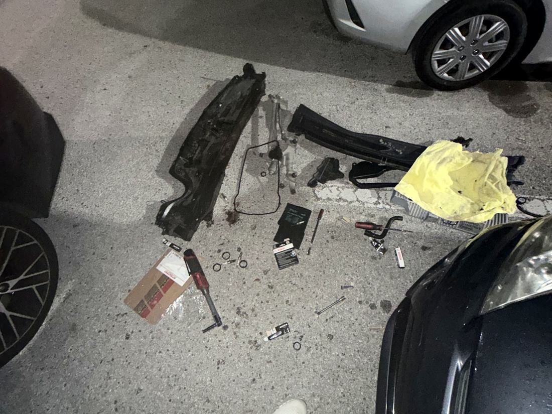 Tools and parts laid out on the pavement beside a customer's car